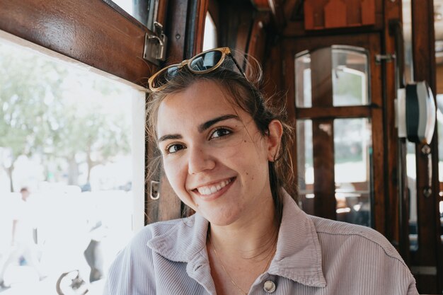 Young woman on sunglasses inside an old train in porto smiling to camera on indie clothes, travel and new experiences concept