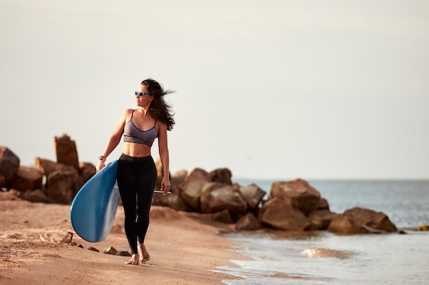 Young woman in sunglasses walking on the beach with a surf front view