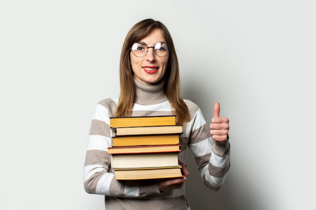 Young woman in a sweater and glasses holding a stack of books