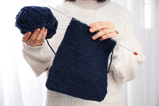 Young woman in sweater holds knitting accessories