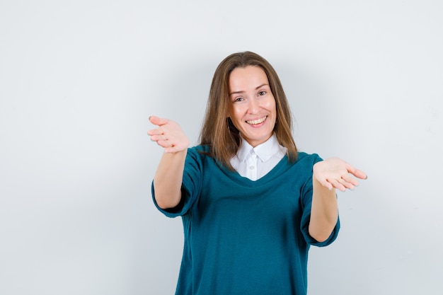 Young woman in sweater over white shirt opening arms for hug and looking happy , front view.