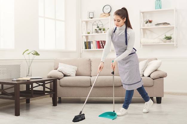 Young woman sweeping house with broom and scoop