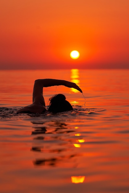 Young woman swimming in the sea on sunrise