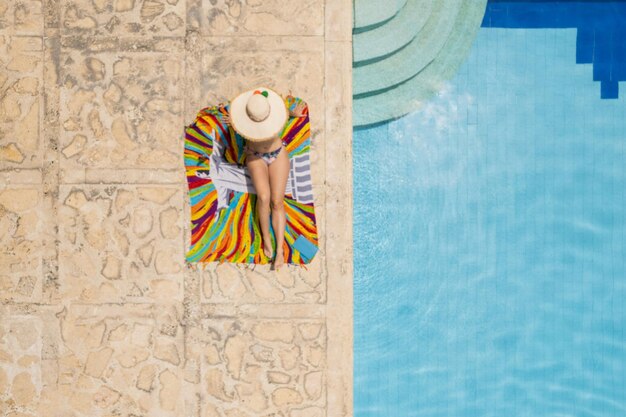 Young woman in swimsuit sunbathing on the pool shore in summer