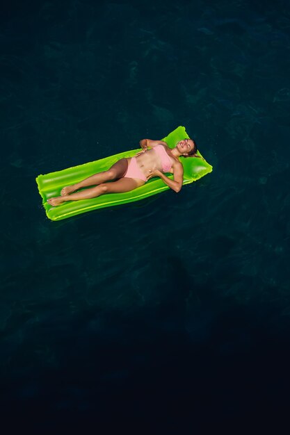 A young woman in a swimsuit swims on an inflatable bright mattress in the sea Summer vacation concept