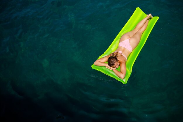 Photo a young woman in a swimsuit swims on an inflatable bright mattress in the sea. summer vacation concept.