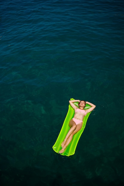 A young woman in a swimsuit swims on an inflatable bright mattress in the sea. Summer vacation concept.