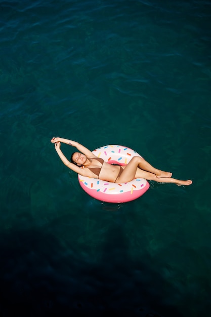 Young woman in a swimsuit swims on an inflatable ring in the sea. Summer vacation concept.