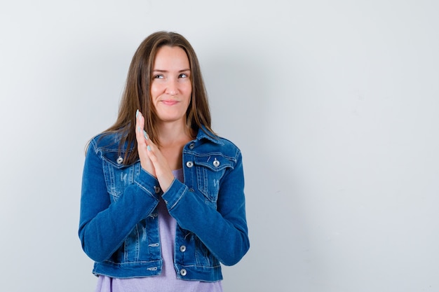 Young woman in t-shirt, jacket rubbing palms together, looking away and looking thoughtful , front view.