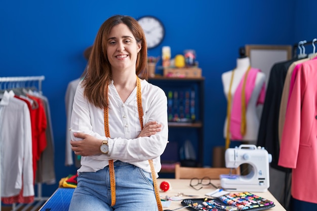 Young woman tailor smiling confident sitting with arms crossed gesture at sewing studio