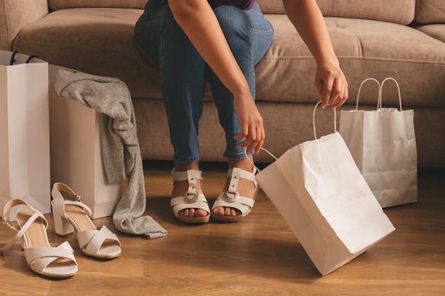 A young woman takes out her purchases from a bag while sitting on the sofa