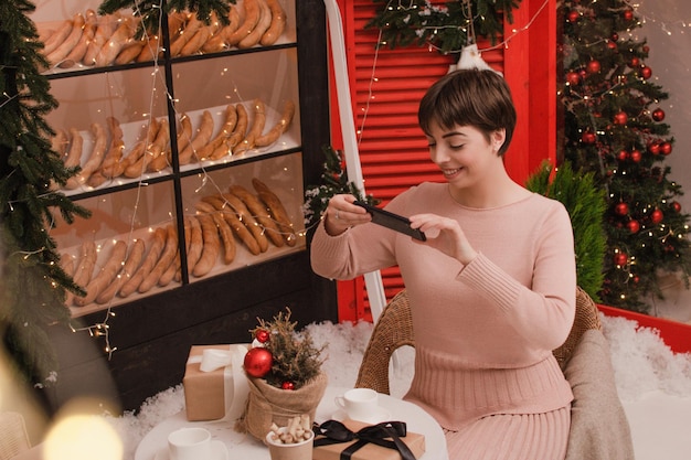 Young woman takes photo gift box on festive table with fir composition, christmas time