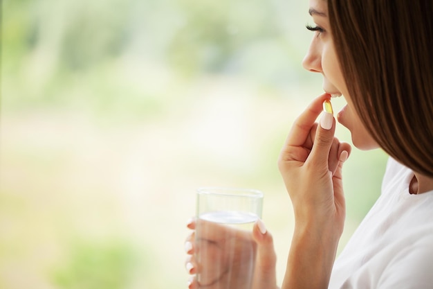 Young woman takes round pill with glass of water in hand