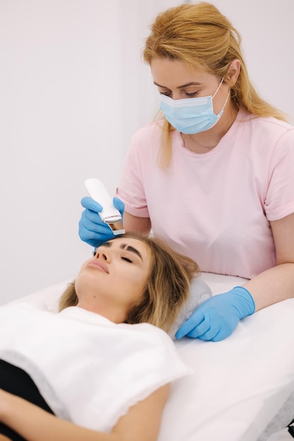 Young woman taking beauty procedure in spa salon beautician using peeling device ultrasonic clining