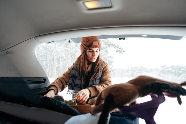 Young woman taking luggage out of car on winter trip