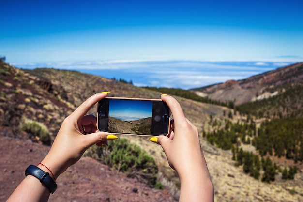 Young woman taking a photo with her phone of amazing mountains landscape on Tenerife Canary islands Spain Travel concept