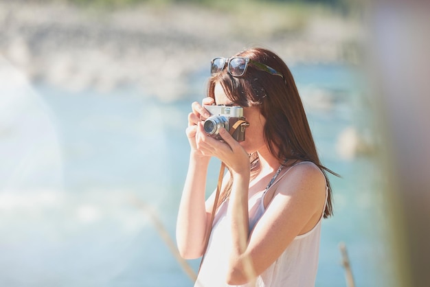 Young woman taking photos of nature on her digital camera during a holiday Young woman on a holiday adventure using her digital camera to take photos of the natural scenery by a river