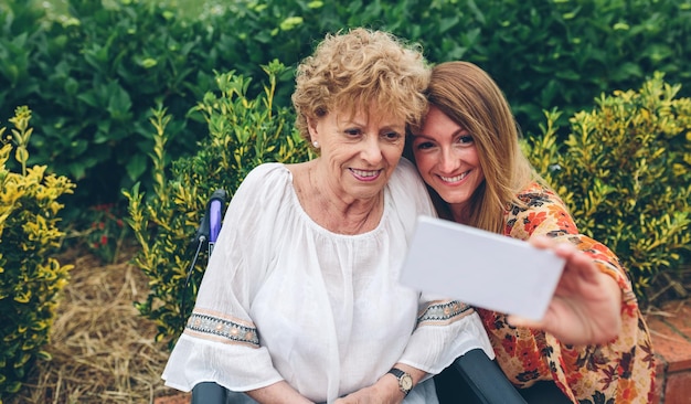 Young woman taking selfie with her older mother in a wheelchair