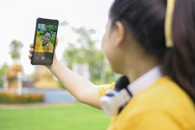 A young woman taking a selfie with a smartphone, wearing a yellow shirt and smiling at the camera, taken from behind.