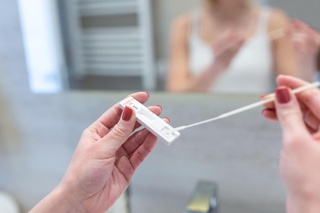 Young woman taking a Selfswabbing home tests for COVID19 at home with Antigen kit Introducing nasal stick to check the infection of Coronavirus Quarantine pandemic