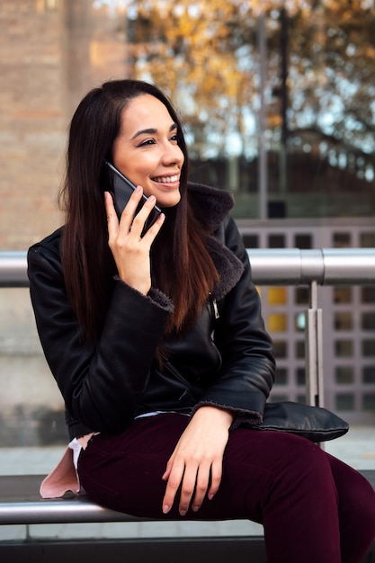 Young woman talking by phone at the bus stop