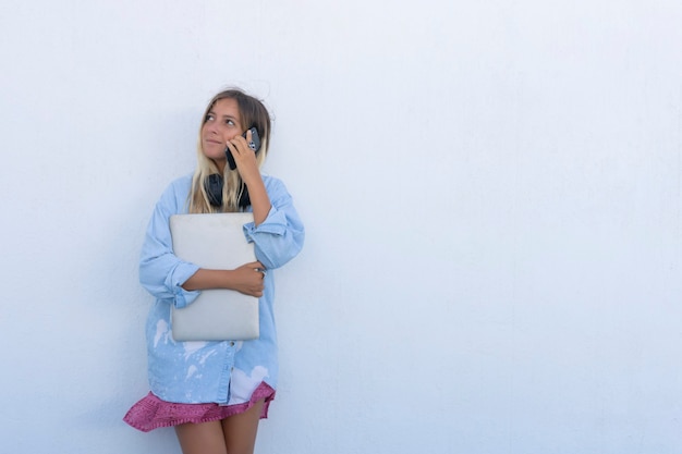 Young woman talking on the phone leaning against a wall