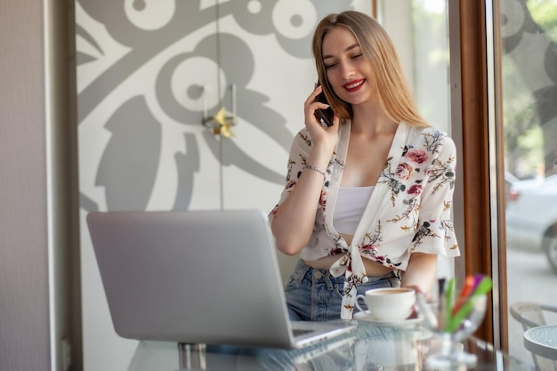 Young woman talking on the phone while sitting at table with laptop in a cafe