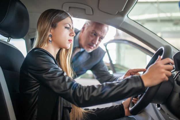 Young woman talking to the salesman to buy her new car in a showroom