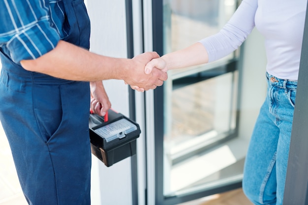 Young woman and technician or plumber with toolbox saying goodbye while shaking hands after repair work