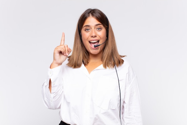 Young woman telemarketer feeling like a happy and excited genius after realizing an idea, cheerfully raising finger, eureka!