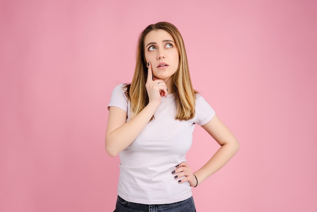 Young woman thinking and looking at copyspace isolated over pink 