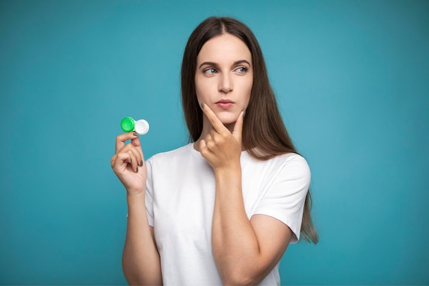 Young woman thoughtfully holding contact lenses