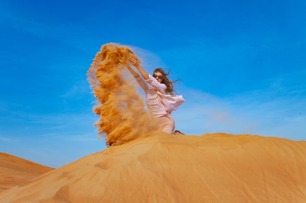 Young woman throwing sand in orande desert