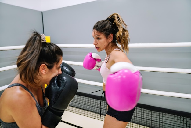 Young woman throwing a side punch to her partner in a boxing practice in the ring