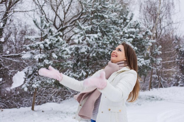 The young woman throws up snow and smiles Woman dressed in warm clothes rejoices outdoors in winter