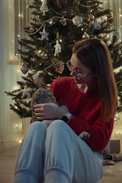 Young woman together with a cat sitting near the Christmas tree Christmas with a pet cat