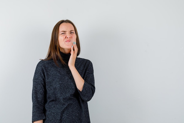 Young woman touching her acne on white background