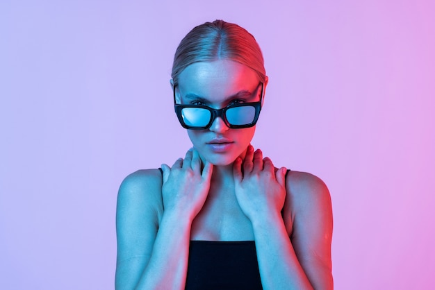 Young woman touching her sunglasses on neon pink