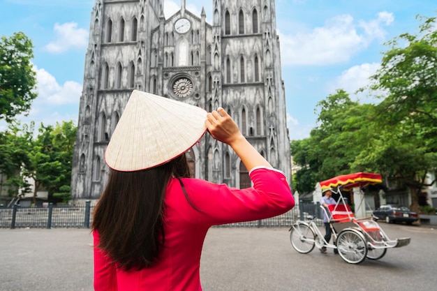 Young woman tourist in Ao Dai traditional Vietnamese dress sightseeing at St Joseph's Cathedra