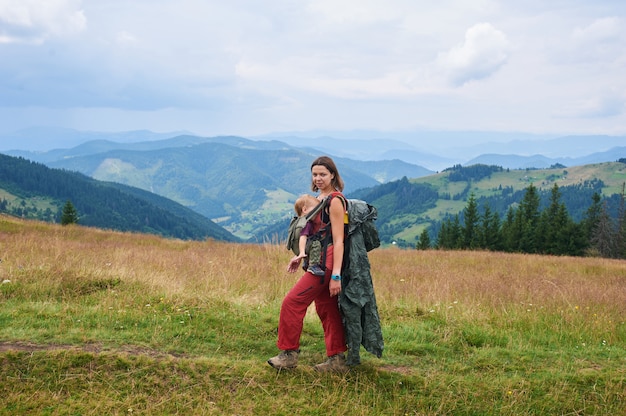 Young woman tourist carrying her little son in ergo baby carrier