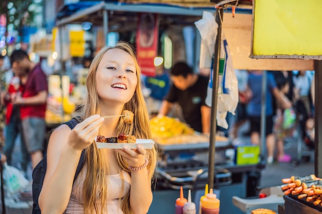 Young woman tourist eating typical korean street food on a walking street of seoul spicy fast food