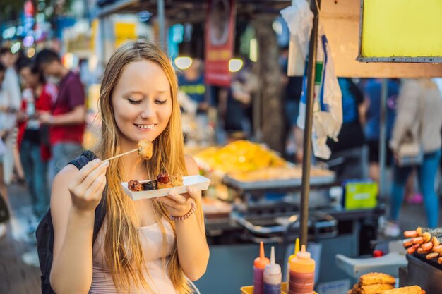 Young woman tourist eating typical korean street food on a walking street of seoul spicy fast food