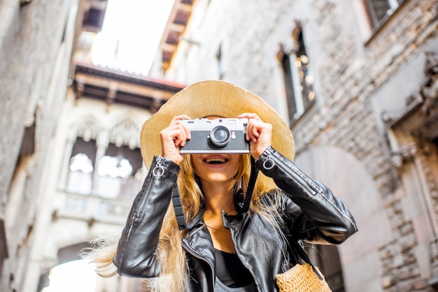 Photo young woman tourist in hat standing with photo camera in front of the famous bridge of sighs in barcelona old town