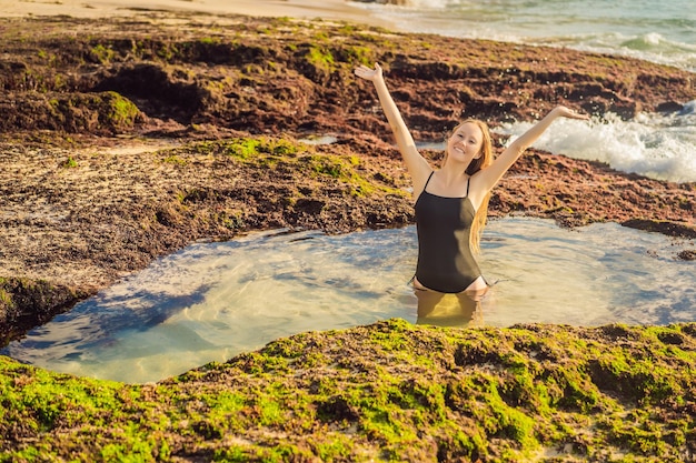 Young woman tourist on Pantai Tegal Wangi Beach sitting in a bath of sea water Bali Island Indonesia Bali Travel Concept