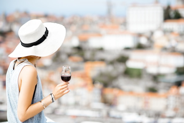 Photo young woman tourist sitting with glass of porto wine on the terrace with great cityscape view on porto city in portugal