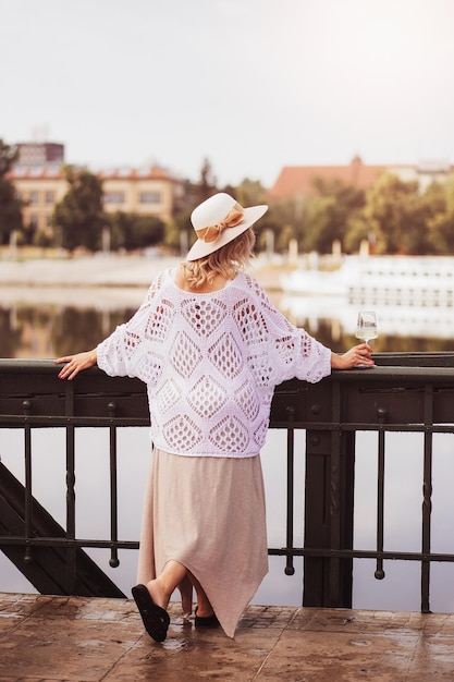 Young woman tourist standing with glass of white wine at bridge in european city river at background