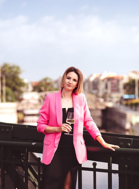 Young woman tourist standing with glass of white wine at bridge in european city river at background