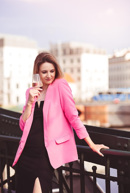 Young woman tourist standing with glass of white wine at bridge in european city river at background