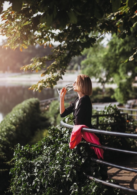 Young woman tourist standing with glass of white wine at bridge in european city river at background