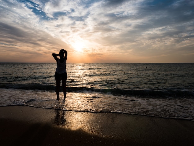 Young woman towards the beautiful sunset on the sea beach. Enjoying the moment